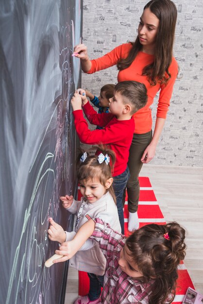 Tutor femenino que dibuja en la pizarra con los niños