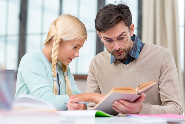 Foto gratuita tutor y niña en casa leyendo un libro