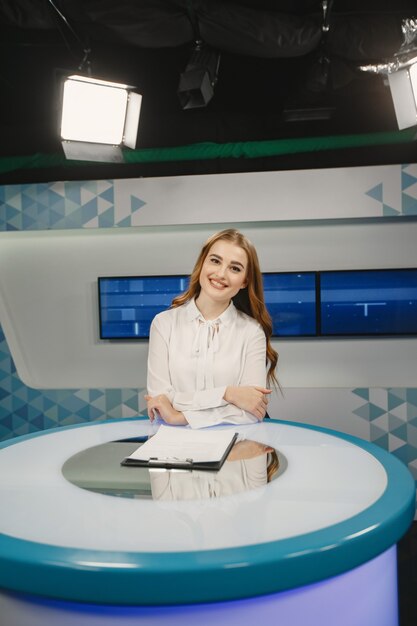 Tv presente en el estudio preparándose para una nueva transmisión. Niña sonriente con camisa blanca sentada en la mesa.