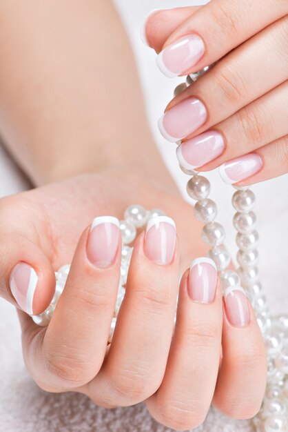 Uñas de mujer hermosa con hermosa manicura francesa y perlas blancas