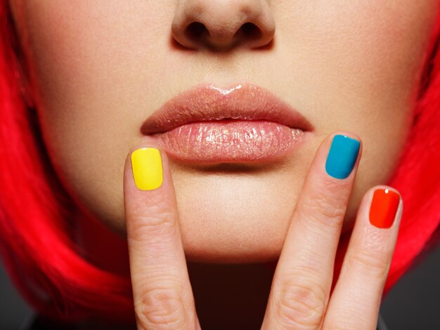 Uñas multicolores cerca de labios de niña de primer plano.