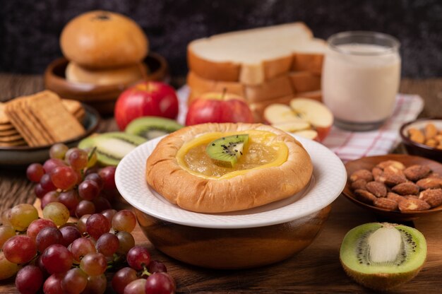 Untar el pan con mermelada y colocarlo con kiwi y uvas La manzana sobre la mesa de madera