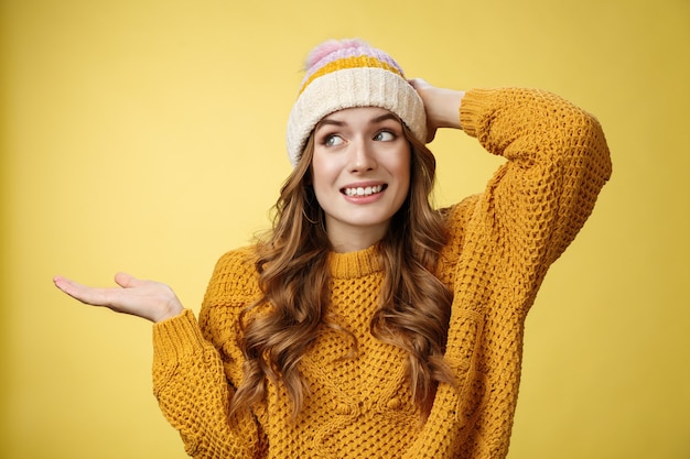 Upsie lo siento. Tonto despreocupado encantador coqueto mujer disculpándose cometiendo un error tonto sonriendo torpe rasguño la cabeza encogiéndose de hombros con la mano hacia los lados, tratando de no mirar a los ojos, de pie fondo amarillo