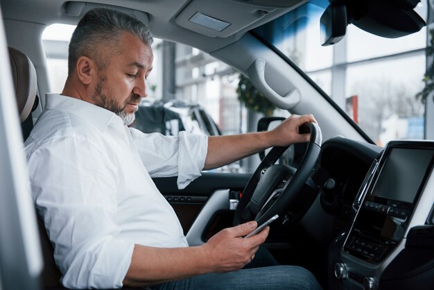 Usando el teléfono móvil. El hombre de negocios se sienta en el automóvil moderno y tiene algunas ofertas