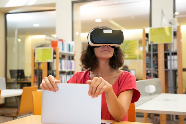 Usuario de biblioteca femenina emocionada que usa simulador de realidad virtual