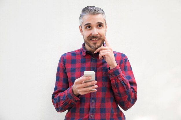 Usuario de teléfono celular pensativo positivo rascándose la barba