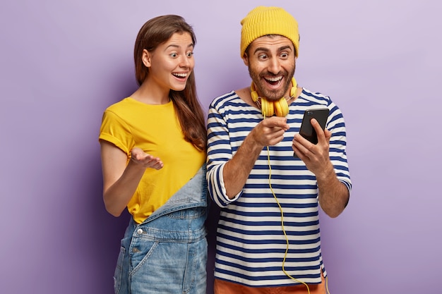 Foto gratuita usuarios femeninos y masculinos jóvenes optimistas de tecnología inteligente, sentirse bien con la actualización exitosa del teléfono celular, mirar la pantalla, consultar el artículo