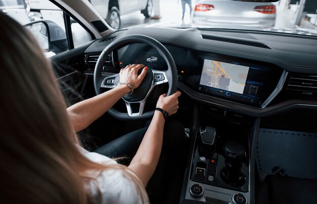 Utilizando GPS. Chica en coche moderno en el salón. Durante el día en interiores. Comprar vehículo nuevo
