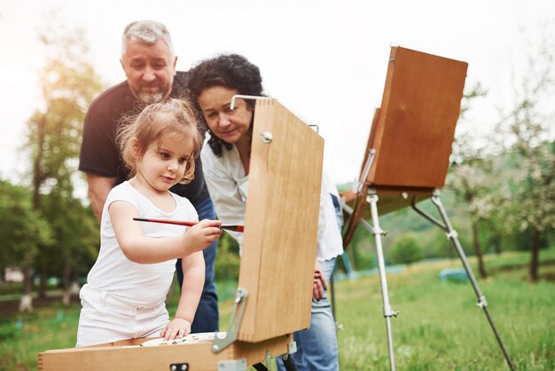 Utilizando un pincel de color rojo. La abuela y el abuelo se divierten al aire libre con su nieta. Concepción de la pintura