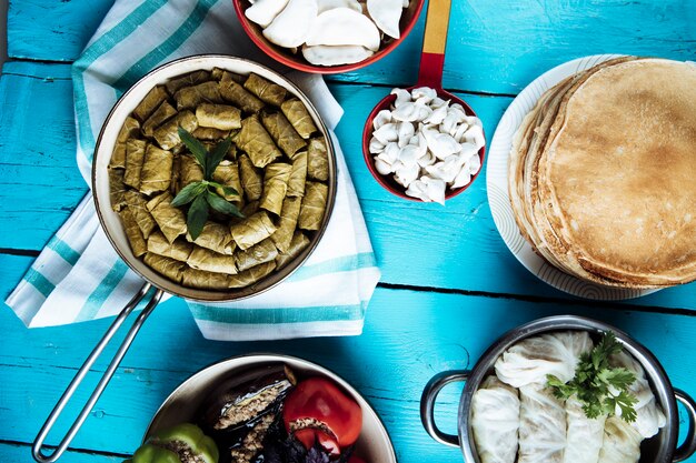 La uva deja dolma, crepes, col dolma en sartenes sobre una mesa azul.