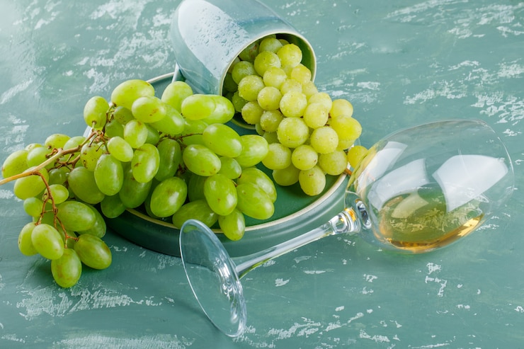 Foto gratuito uvas con bebida en una taza sobre yeso y bandeja de fondo, vista de ángulo alto.