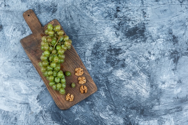 Uvas blancas laicas planas, nueces sobre tabla de cortar sobre fondo de mármol azul oscuro. espacio libre horizontal para su texto