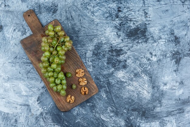 Uvas blancas laicas planas, nueces sobre tabla de cortar sobre fondo de mármol azul oscuro. espacio libre horizontal para su texto