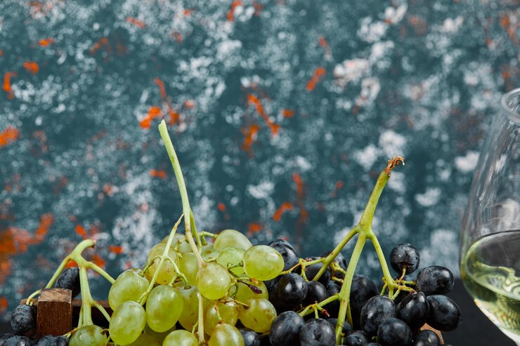 Foto gratuito uvas blancas y negras con una copa de vino sobre fondo azul. foto de alta calidad