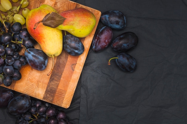 Uvas; ciruela; peras en tabla de cortar de madera