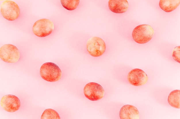 Las uvas se extienden al azar sobre la superficie rosa
