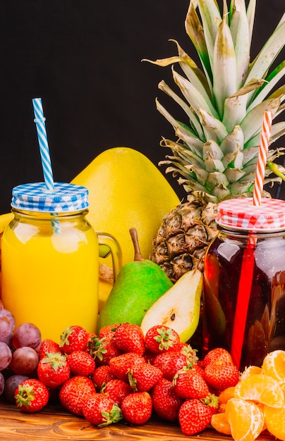 Uvas; fresas; peras; Botella de piña y jugo sobre fondo negro