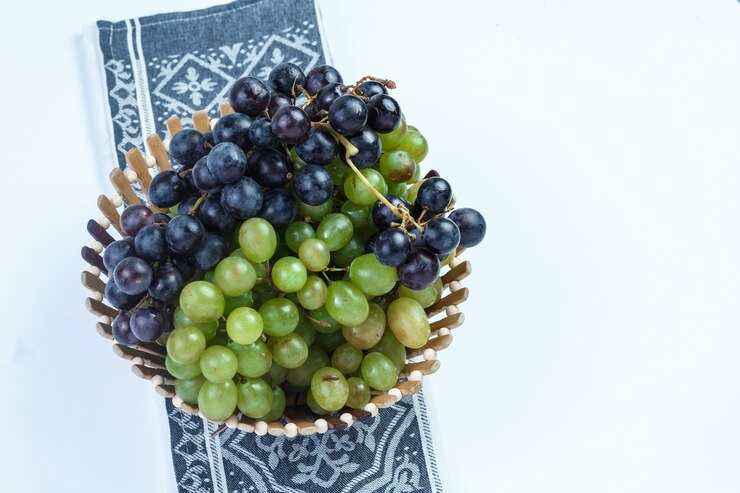 Foto gratuito uvas frescas en una canasta sobre fondo blanco y toalla de cocina. vista de ángulo alto.