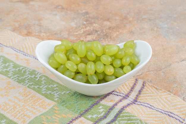 Uvas frescas en tazón de fuente blanco sobre mantel. Foto de alta calidad