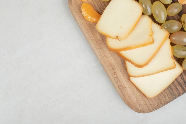 Uvas, mandarinas y queso sobre tabla de madera