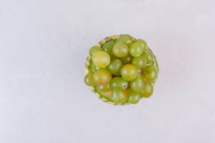 Foto gratuito uvas en medio melón verde cortado sobre superficie blanca