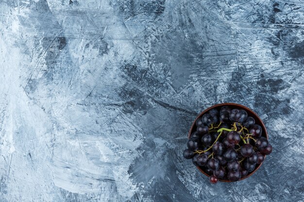 Uvas negras en un cuenco de arcilla plana yacía sobre un fondo de yeso sucio