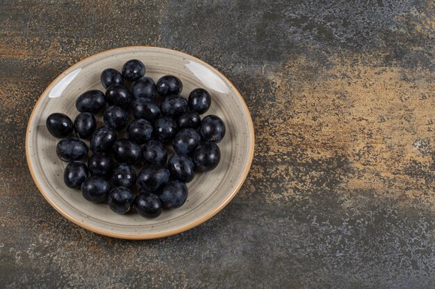 Uvas negras frescas en placa de cerámica.