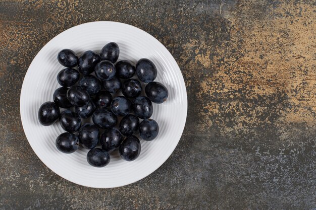 Uvas negras frescas en un plato blanco.