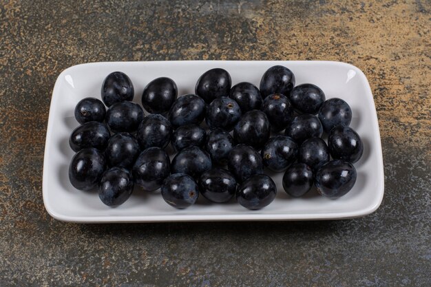 Uvas negras frescas en plato cuadrado blanco.