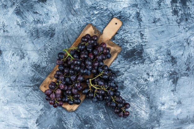 Uvas negras laicas planas sobre yeso sucio y fondo de tabla de cortar. horizontal