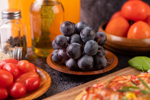Uvas negras en un plato de madera con tomates Zumo de naranja y pizza.