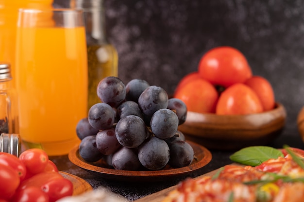 Uvas negras en un plato de madera con tomates Zumo de naranja y pizza.