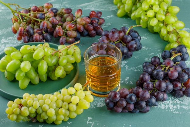 Uvas orgánicas en una bandeja con bebida vista de ángulo alto sobre un fondo de yeso