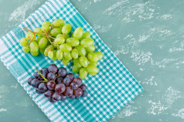 Uvas planas yacen sobre yeso y fondo de tela de picnic