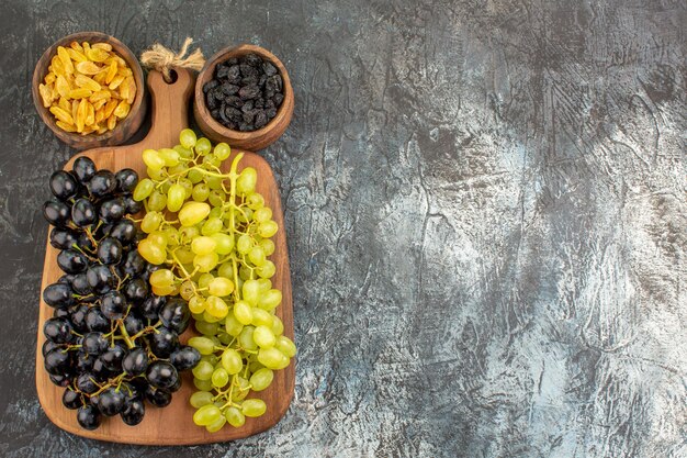 Uvas racimos de uvas en la placa de madera entre dos tazones de frutos secos