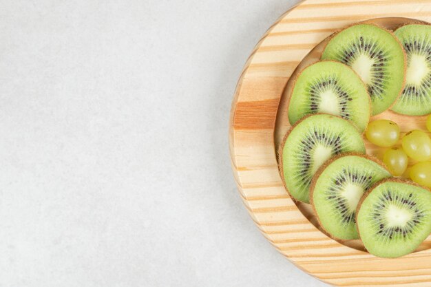 Foto gratuita uvas y rodajas de kiwi en placa de madera