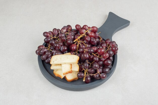 Foto gratuita uvas rojas frescas y rebanadas de queso en tablero oscuro.