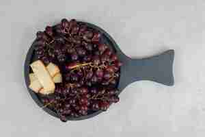 Foto gratuita uvas rojas frescas y rodajas de queso en tablero oscuro