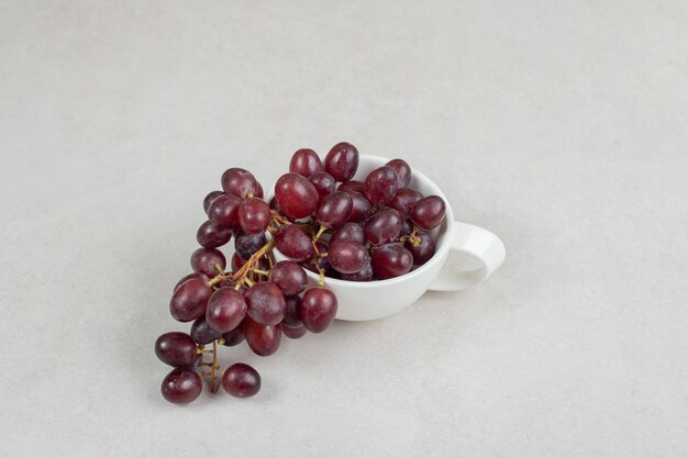 Uvas rojas frescas en taza blanca.
