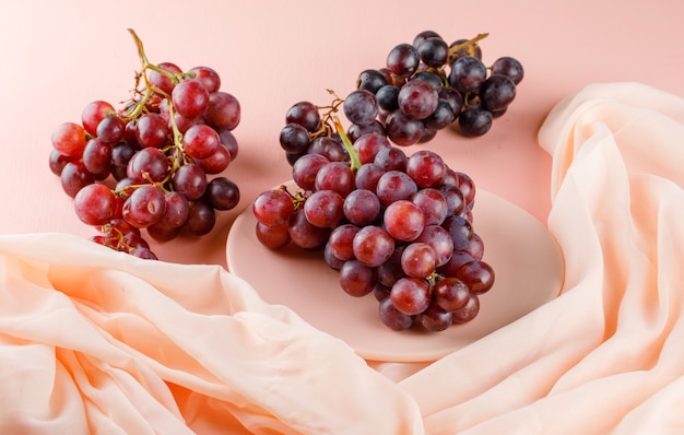 Uvas rojas en un plato sobre rosa y textil. vista de ángulo alto.