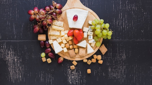 Foto gratuita uvas rojas y verdes, tomates, queso y pastelería sobre fondo negro con textura