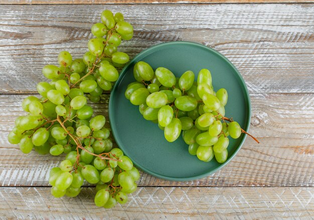 Uvas verdes en una bandeja sobre un fondo de madera. endecha plana.