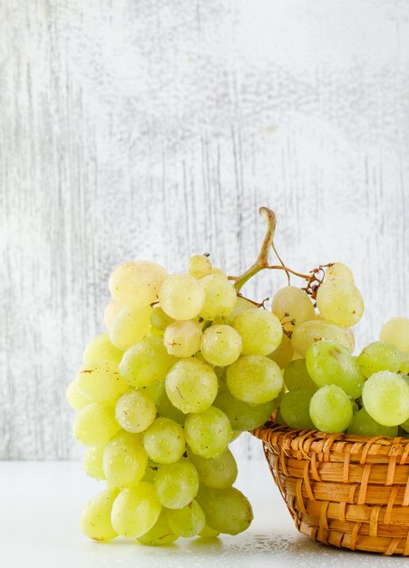 Uvas verdes en una canasta de mimbre en blanco y sucio, primer plano.