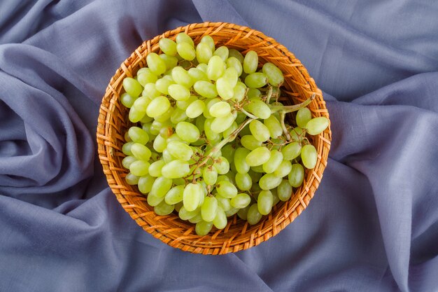 Uvas verdes en una canasta de mimbre sobre textiles,