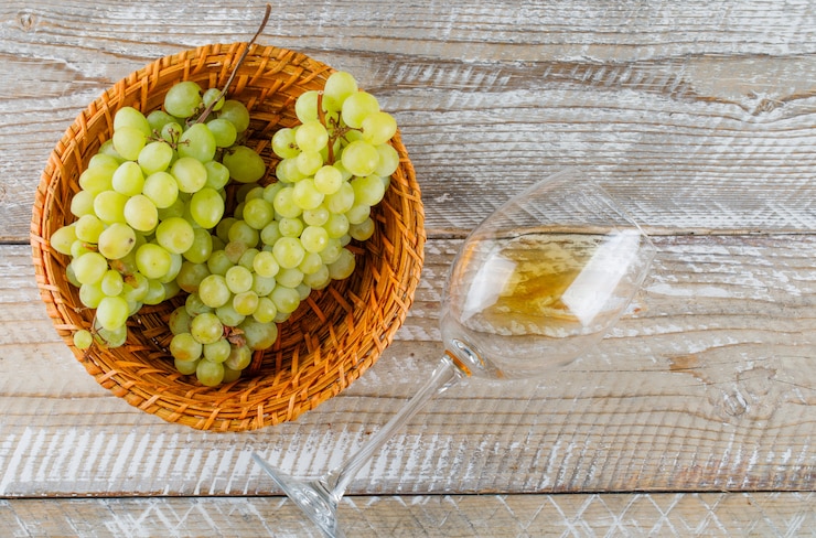 Foto gratuito uvas verdes en una cesta de mimbre con bebida plana yacía sobre un fondo de madera