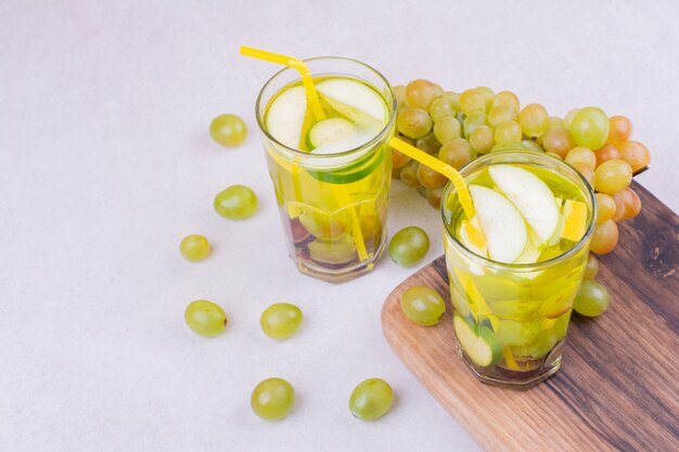 Uvas verdes con dos vasos de jugo en una tabla de madera