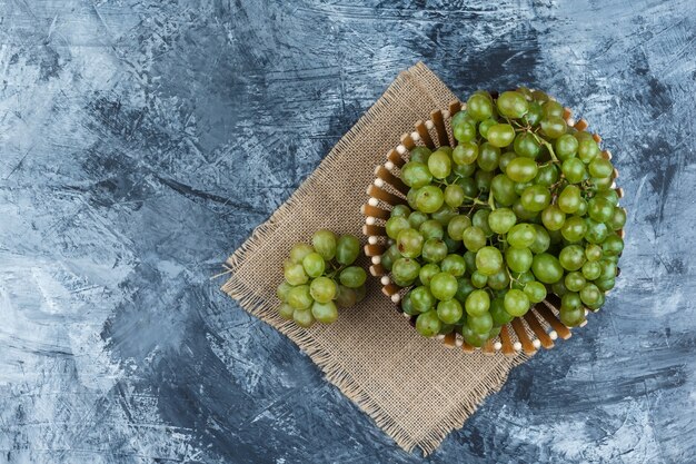 Uvas verdes laicos planas en canasta sobre grunge y pedazo de fondo de saco. horizontal