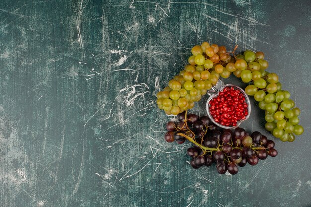 Uvas verdes y negras con semillas de granada sobre superficie de mármol.