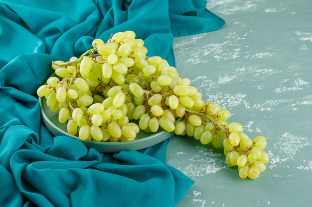 Uvas verdes en una placa de vista de ángulo alto en yeso y textiles
