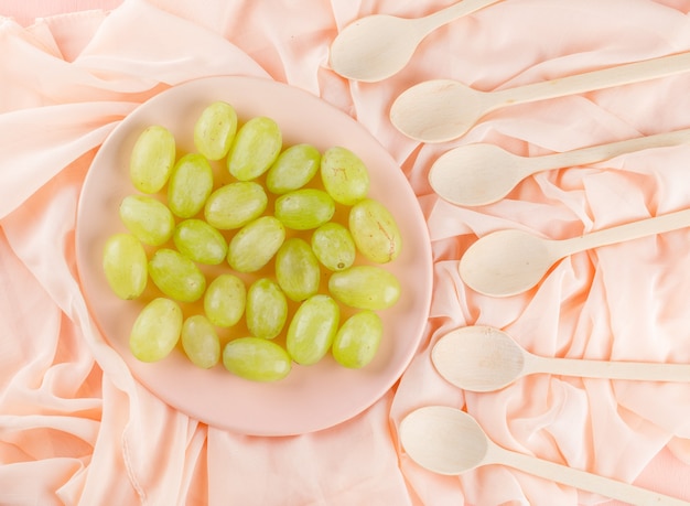 Las uvas verdes en un plato con cucharas de madera planas yacían sobre un tejido rosa